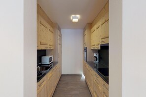 Una cocina estrecha con armarios de madera, un microondas, una cafetera y una encimera negra.