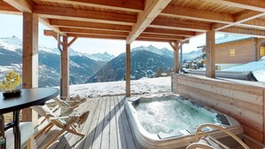 A wooden deck with a hot tub and seating, overlooking snow-covered mountains. - Lush chalet in Heremence with sauna (Hérémence)