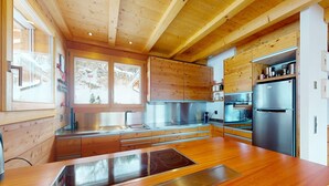 A modern kitchen with wooden cabinets, stainless steel appliances, and a large window. - Lush chalet in Heremence with sauna (Hérémence)