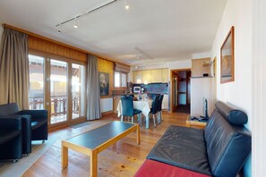 A modern living room with a sofa, a dining table, and a kitchen in the background. - Apartment with front balcony (Veysonnaz)