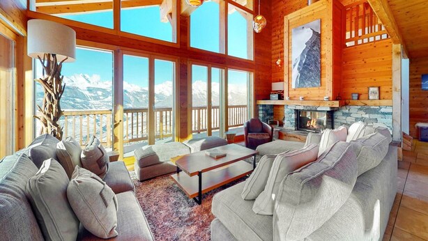 Un salón amplio con chimenea, ventanas grandes y vistas a montañas nevadas.
