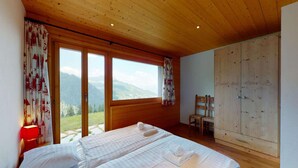 A bedroom with a wooden ceiling, large windows with a mountain view, a bed with white linens, and a wooden wardrobe. - Apartment in Nendaz on ski slopes (Haute-Nendaz)