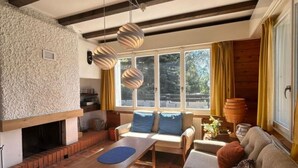 Una sala de estar acogedora con chimenea, un sofá, una mesa de centro y un amplio ventanal con cortinas.