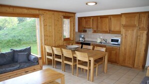 Una habitación acogedora con una mesa de comedor de madera, sillas, un sofá y una zona de cocina con armarios de madera y un ventanal.