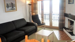 Una sala de estar con un sofá negro, una mesa de centro de madera, un sillón negro y una chimenea.