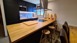 Cocina moderna con armarios oscuros, encimera de madera, campana extractora de acero inoxidable y ventana con vistas.