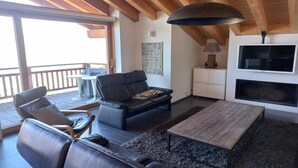Una sala moderna con techo de madera, un sofá de cuero negro, una mesa de centro de madera y un televisor montado en la pared.