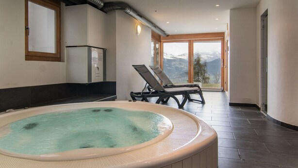 Un área de spa con hidromasaje, sillones de descanso y vistas a las montañas.