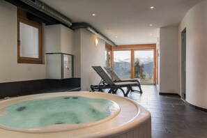 A spa area with a hot tub, lounge chairs, and a view of mountains.