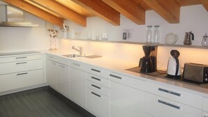 Una cocina moderna con armarios blancos, techo de madera y encimera con cafetera, tostadora y frascos de vidrio.