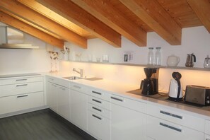 A modern kitchen with white cabinets, a wooden ceiling, and a countertop with a coffee maker, toaster, and glass jars.