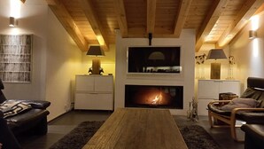Un salón acogedor con chimenea, vigas de madera en el techo y una moderna repisa para la chimenea.