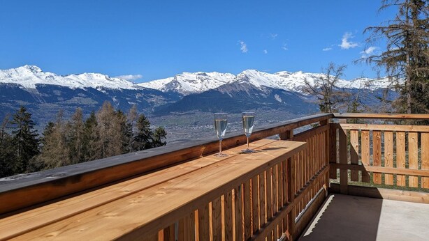 A wooden deck with two glasses of water, overlooking snow-capped mountains and a clear blue sky. - Modern apartment with balcony, ski access (Veysonnaz)