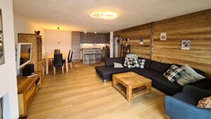 A modern living room with a dark sofa, wooden coffee table, and a dining area with chairs and a table. - Modern apartment with balcony, ski access (Veysonnaz)