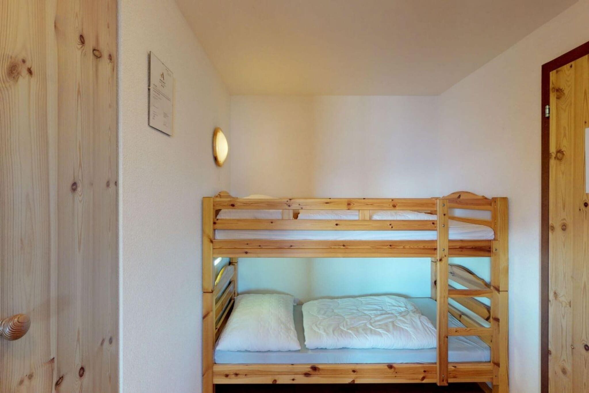 Habitación con literas, paredes de madera y una lámpara pequeña sobre la cama.