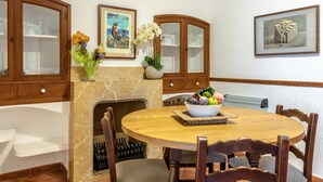 A dining area with a round wooden table, chairs, a fireplace, and a fruit bowl.