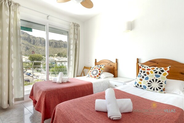 A hotel room with two beds, a large window with curtains, and a view of a mountainous landscape.