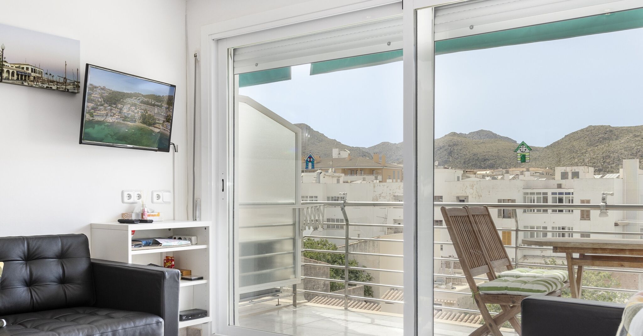 A modern room with a balcony, a black leather chair, a wooden chair, and a TV mounted on the wall.