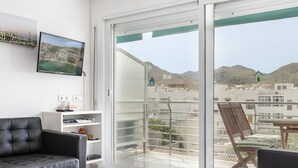 A modern room with a balcony, a black leather chair, a wooden chair, and a TV mounted on the wall.