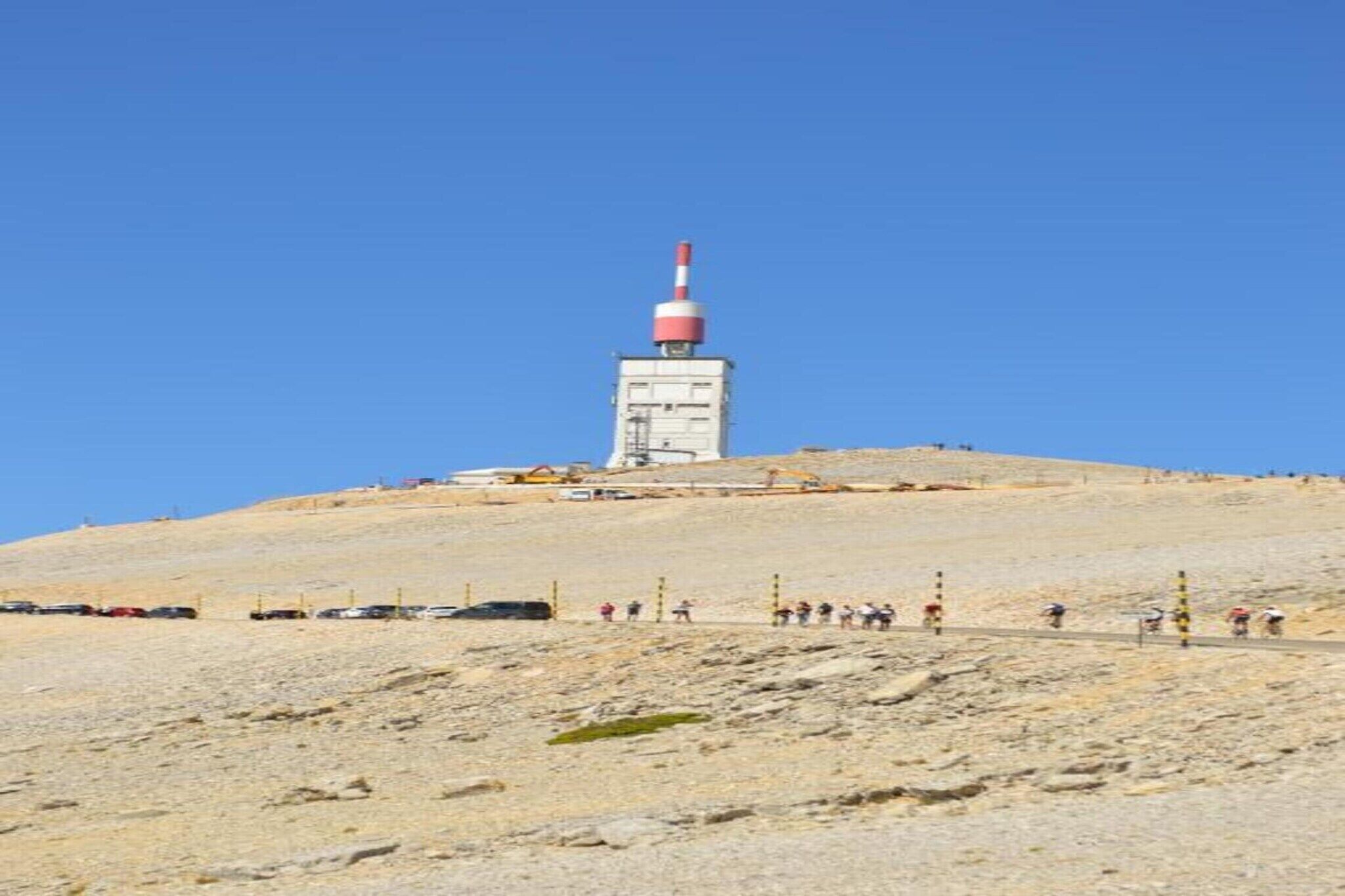A hilltop with a tall structure featuring a red and white top, surrounded by a clear blue sky.