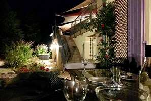 Ein Essbereich im Freien mit einem Tisch für zwei Personen, eine Treppe zu einer erhöhten Ebene und eine überdachte Sitzgelegenheit.
