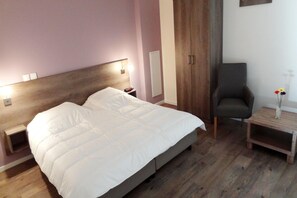 Ein Schlafzimmer mit einem großen Bett, einem Nachttisch, einem Sessel und einem kleinen Tisch mit einer Vase.