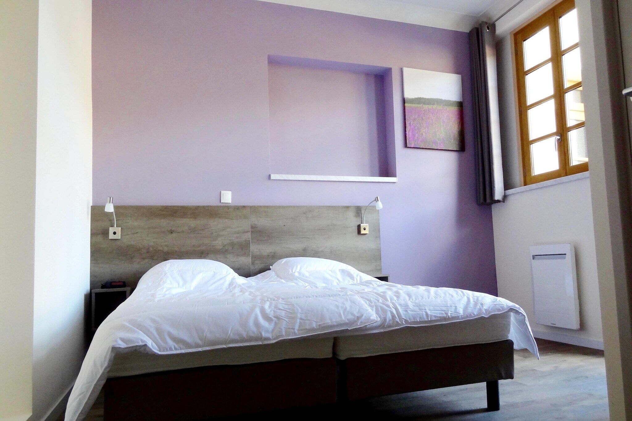Een slaapkamer met een bed, nachtkastje, wandplank, raam met gordijnen en een radiator.