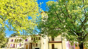 A two-story building with a balcony on the second floor, surrounded by trees. - Château Comfort in Provence (Ferrassières)