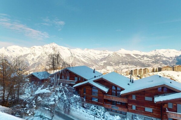 A wooden lodge with multiple balconies, set against a backdrop of snow-covered mountains.