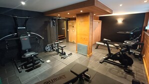 Ein Heimfitnessraum mit verschiedenen Trainingsgeräten, darunter eine Hantelbank, Kurzhanteln und ein Laufband.