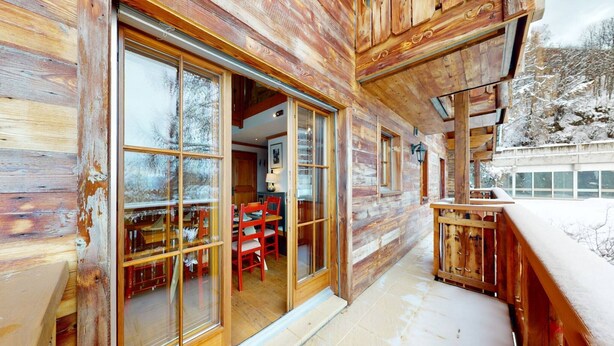 Eine Holzhütte mit großen Glasüren, die in einen Essbereich mit roten Stühlen und einem Tisch führen.