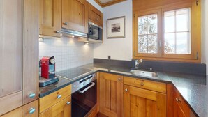 Eine Küche mit Holzausstattung, einer Mikrowelle, einem Backofen, einer Kaffeemaschine, einem Spülbecken und einem Fenster mit Blick auf Bäume.