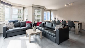 A modern living room with a large L-shaped black leather sofa, a wooden coffee table, and a dining area with a wooden table and black chairs. - Apartment in Ostend near Sandy Beaches (Oostende)