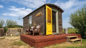 A wooden cabin with a yellow door, a deck, and a sign that reads "CAMPER". - Apartment in Netherlands near the Coast ('t Zand)
