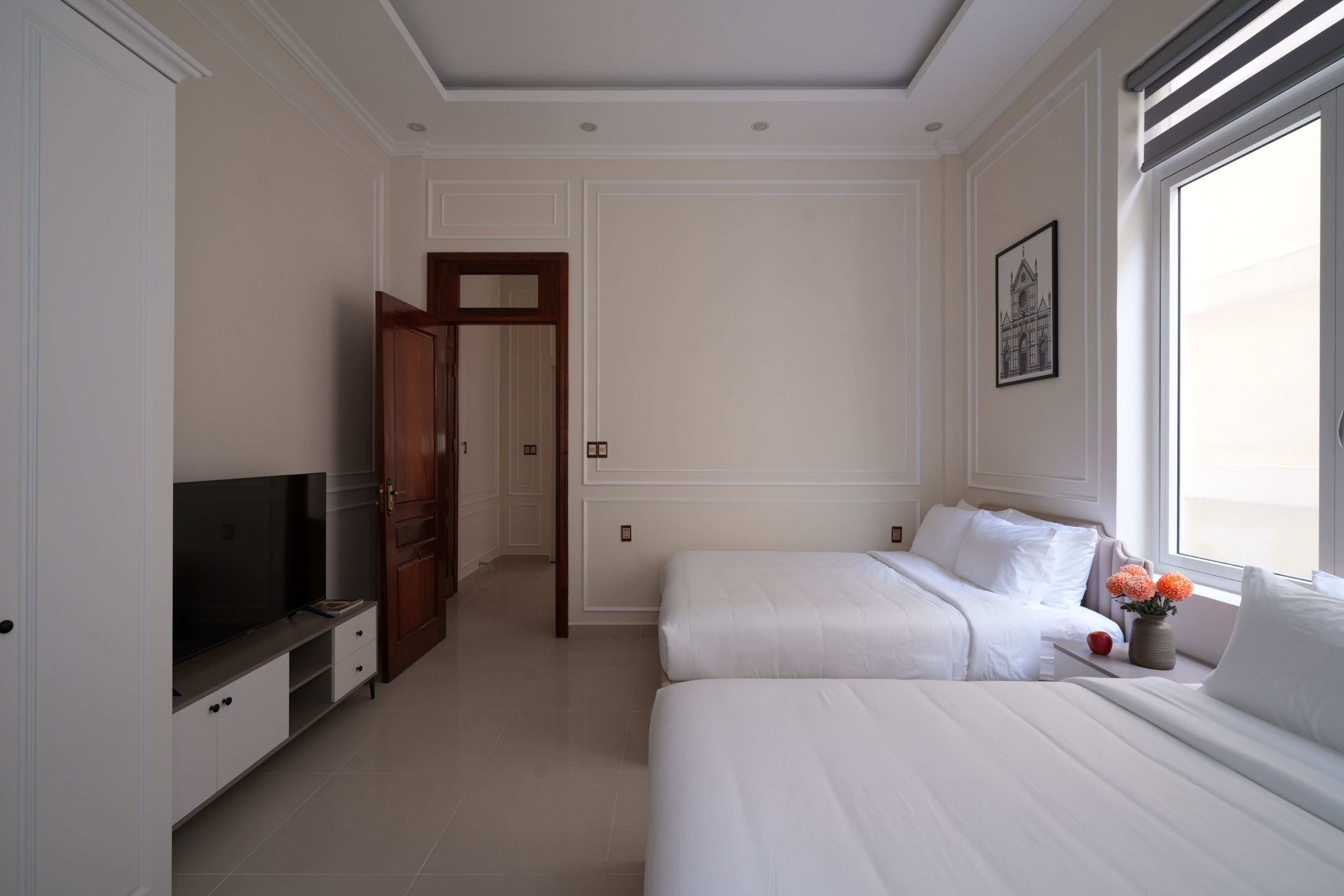 A hotel room with two beds, a TV, a wooden door, and a window with a view.