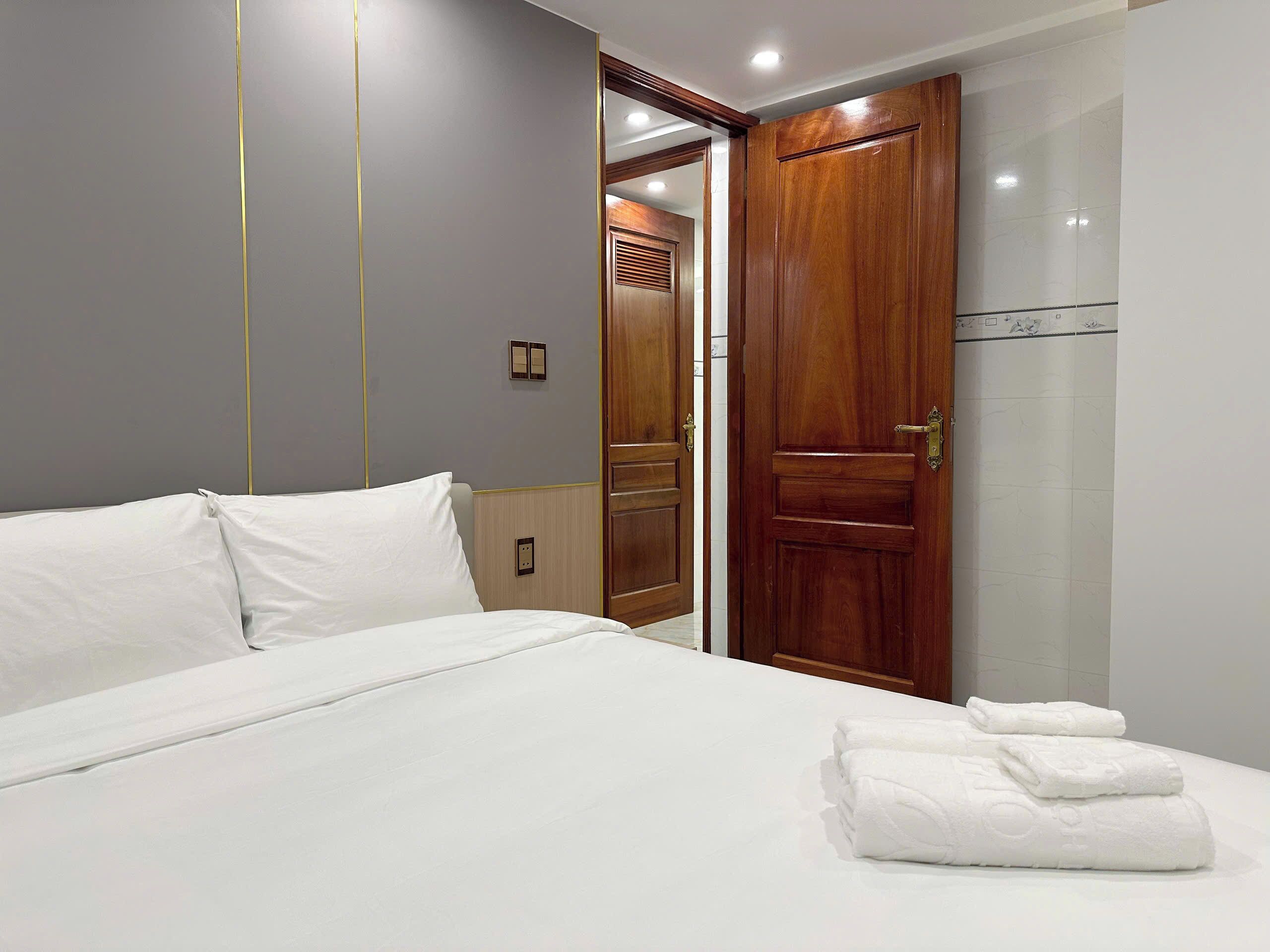 A hotel room with a neatly made bed, a wooden door, and a bathroom visible through a glass partition.