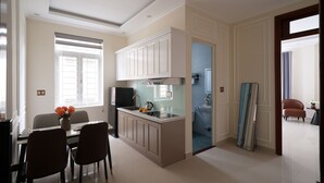 A modern kitchen with white cabinets, a dining area with a table and chairs, and a view into the adjacent bathroom. - The One Da Lat Hotel (Xuan Huong - Da Lat)