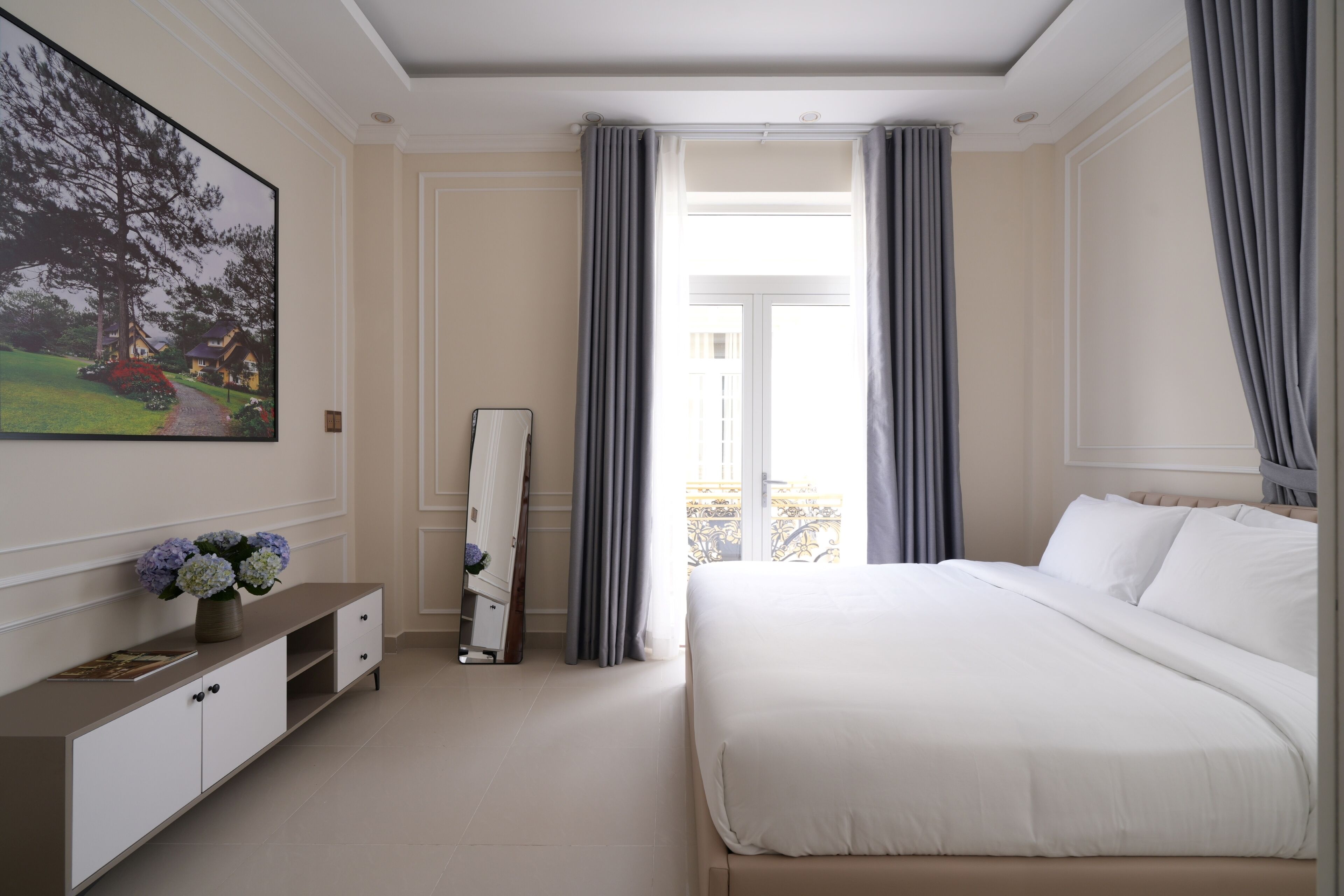 A modern hotel room with a large bed, a flat-screen TV, a vanity with a mirror, and a view of the outdoors.