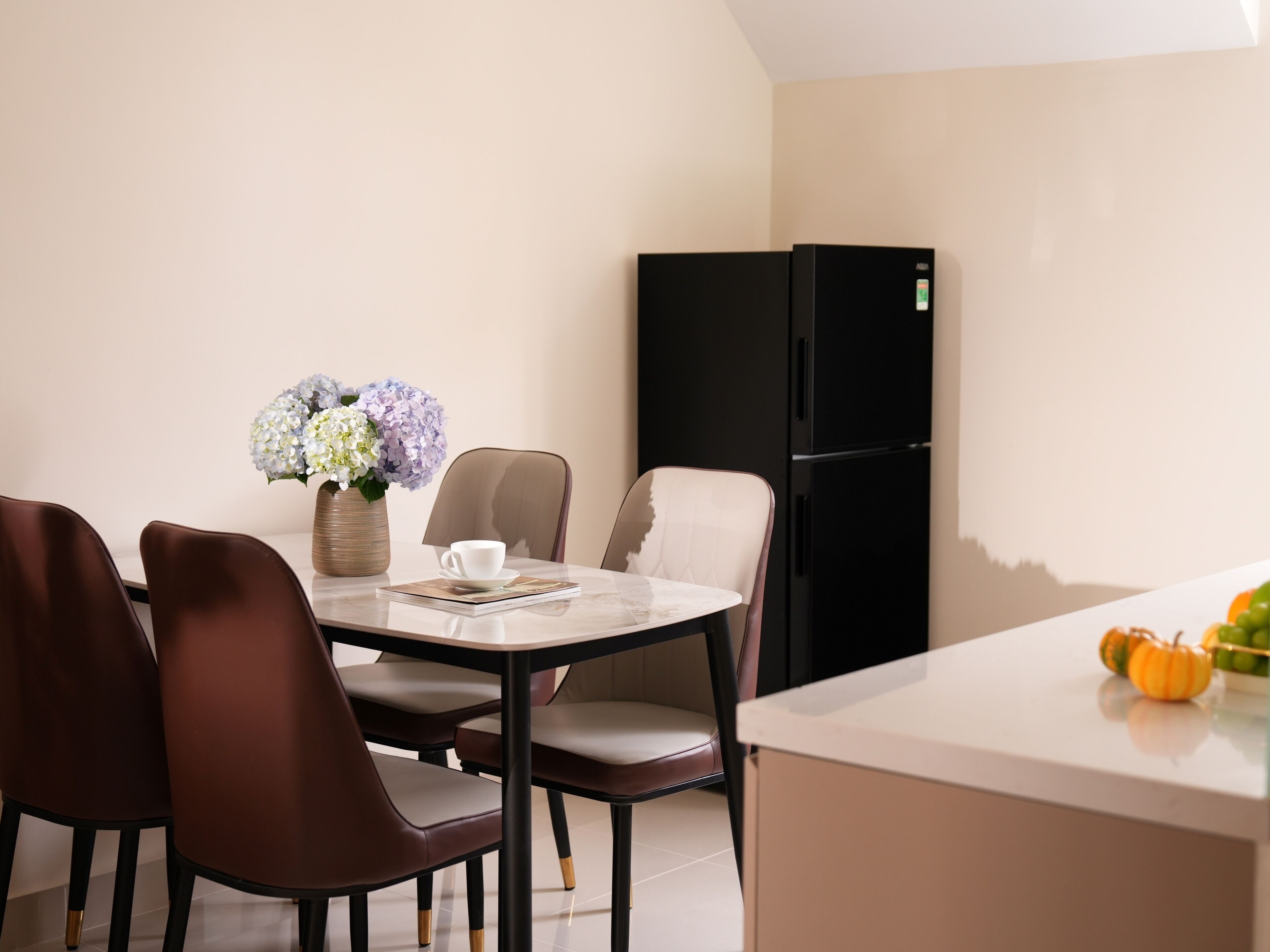 A modern dining area with a round table, four chairs, a vase with flowers, and a black refrigerator.