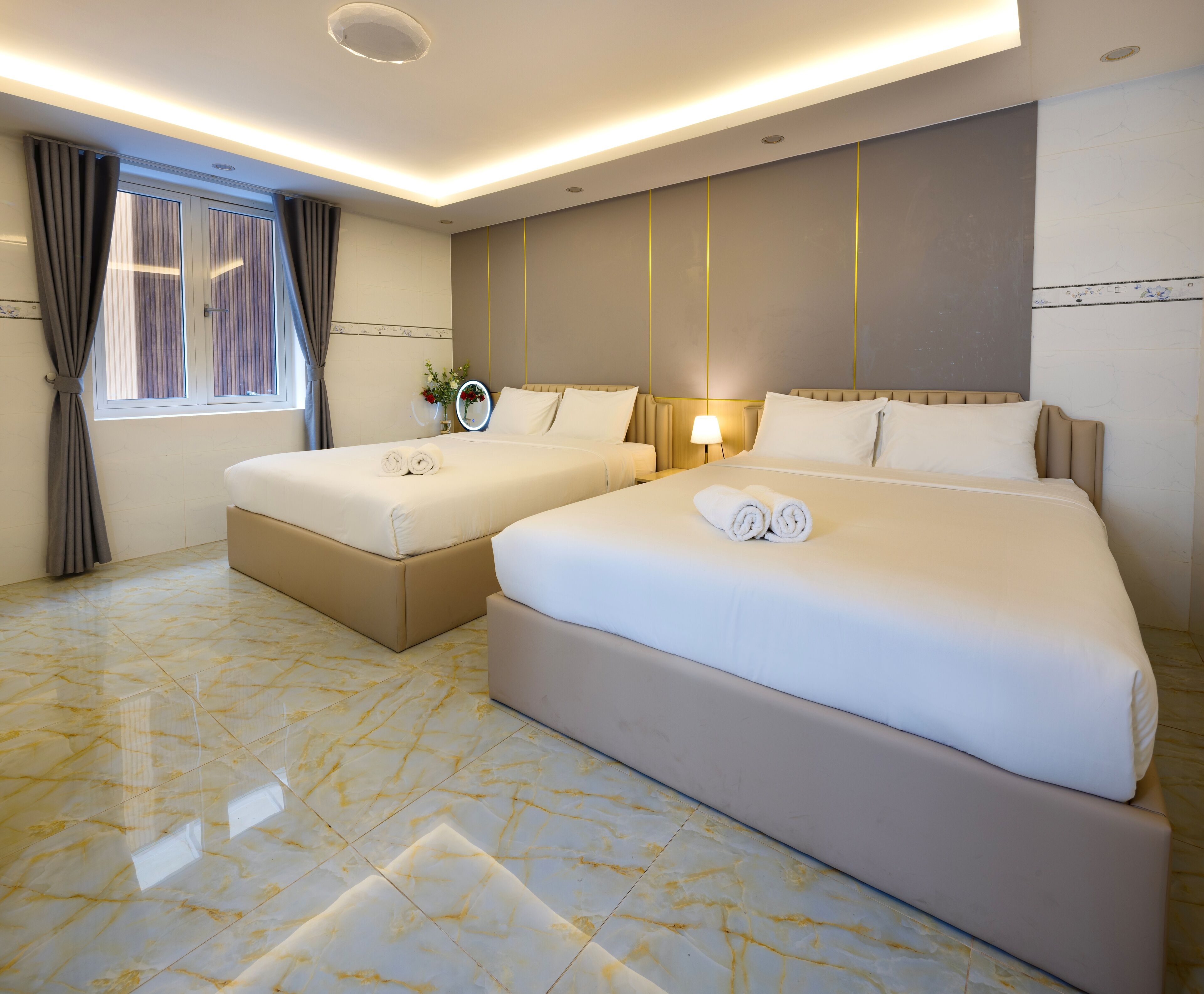 A hotel room with two beds, a vanity with a mirror, and a window with curtains.