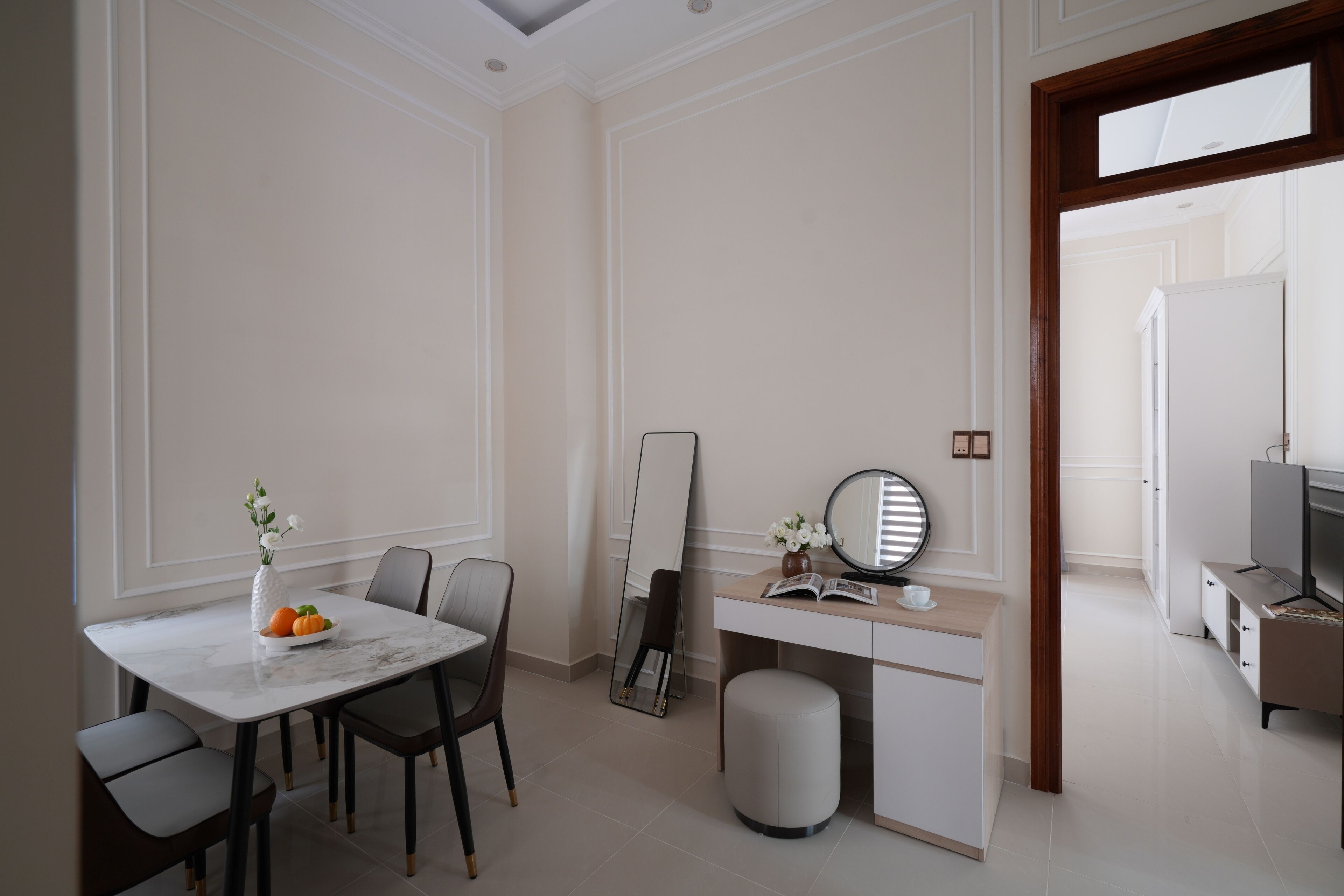 A modern hotel room with a dining area, a vanity with a mirror, and a television.