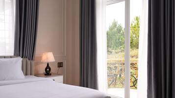 Una habitación de hotel con una cama, una mesita de noche con lámpara y vistas a un balcón con mobiliario exterior.