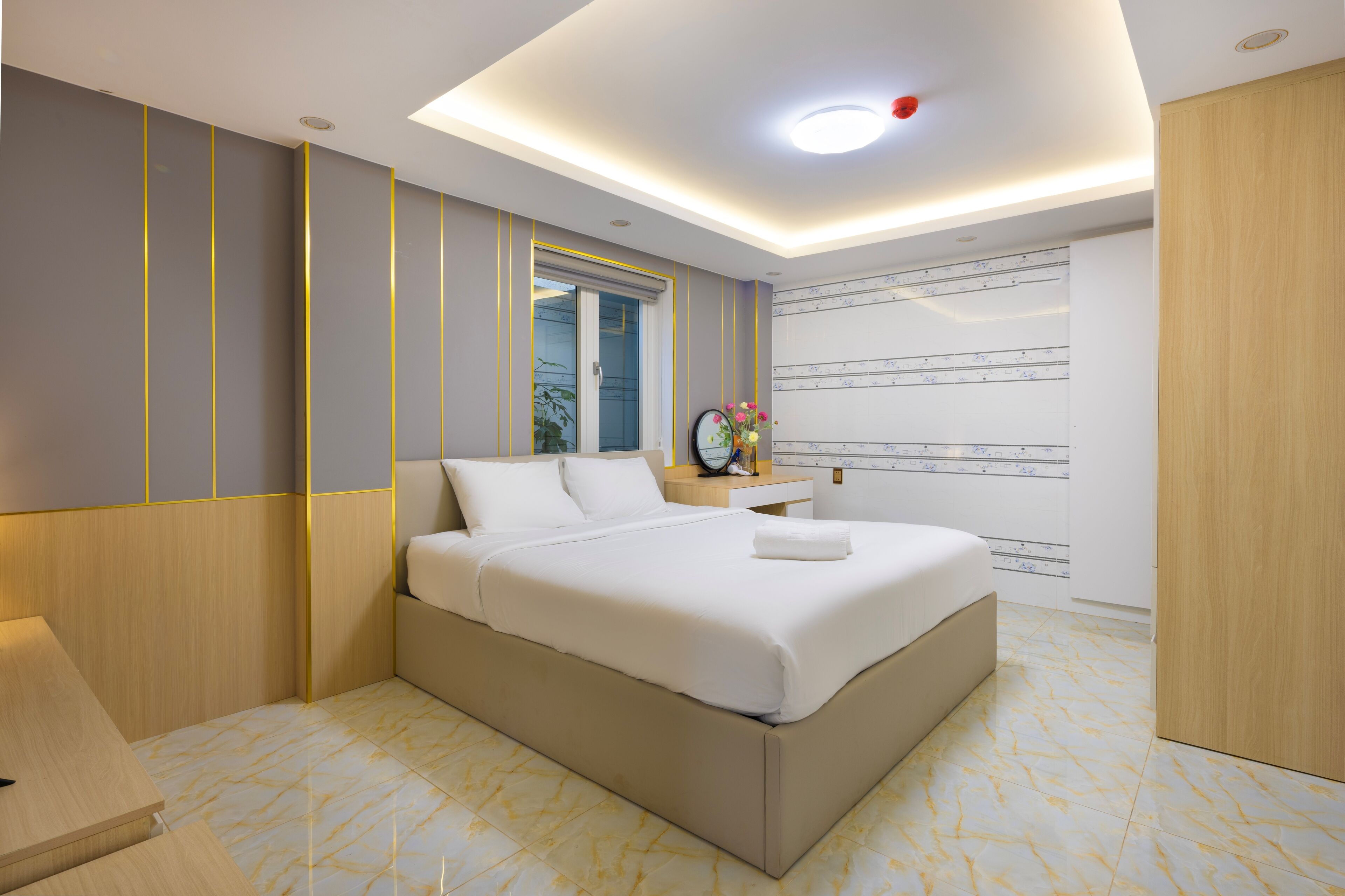 A modern hotel room with a large bed, a bedside table, a nightstand, a mirror, and a wall with a decorative pattern.