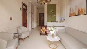 A hotel lobby with a reception desk, a chandelier, a sofa, and a small table with flowers. - The One Da Lat Hotel (Xuan Huong - Da Lat)