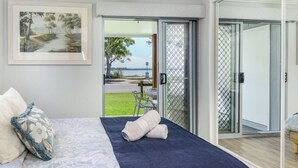 A bedroom with a bed, pillows, a view of the outdoors, and a sliding glass door leading to a patio area.
