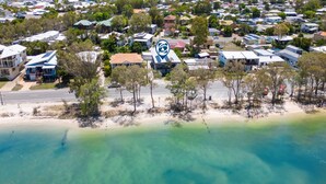 An aerial view of a coastal residential area with houses, a beach, and a clear road.
