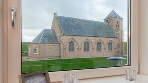 A view of a church with a clock tower and a smaller building, through a window with a picture frame and two clear glass vases on the windowsill. - Holiday Home in Zoutelande near Sandy Beaches (Zoutelande)