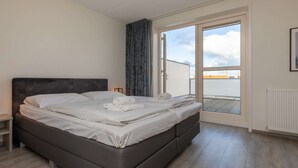 A modern bedroom with a large bed, a nightstand, and a view through a sliding glass door to an outdoor balcony. - Holiday Home in Zoutelande near Sandy Beaches (Zoutelande)
