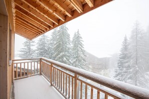 Ein Holzbalkon mit schneebedeckter Brüstung, mit Blick auf ein Gebäude und schneebedeckte Bäume.