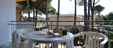 A balcony with a table set for two, a chair, and a view of trees and buildings.